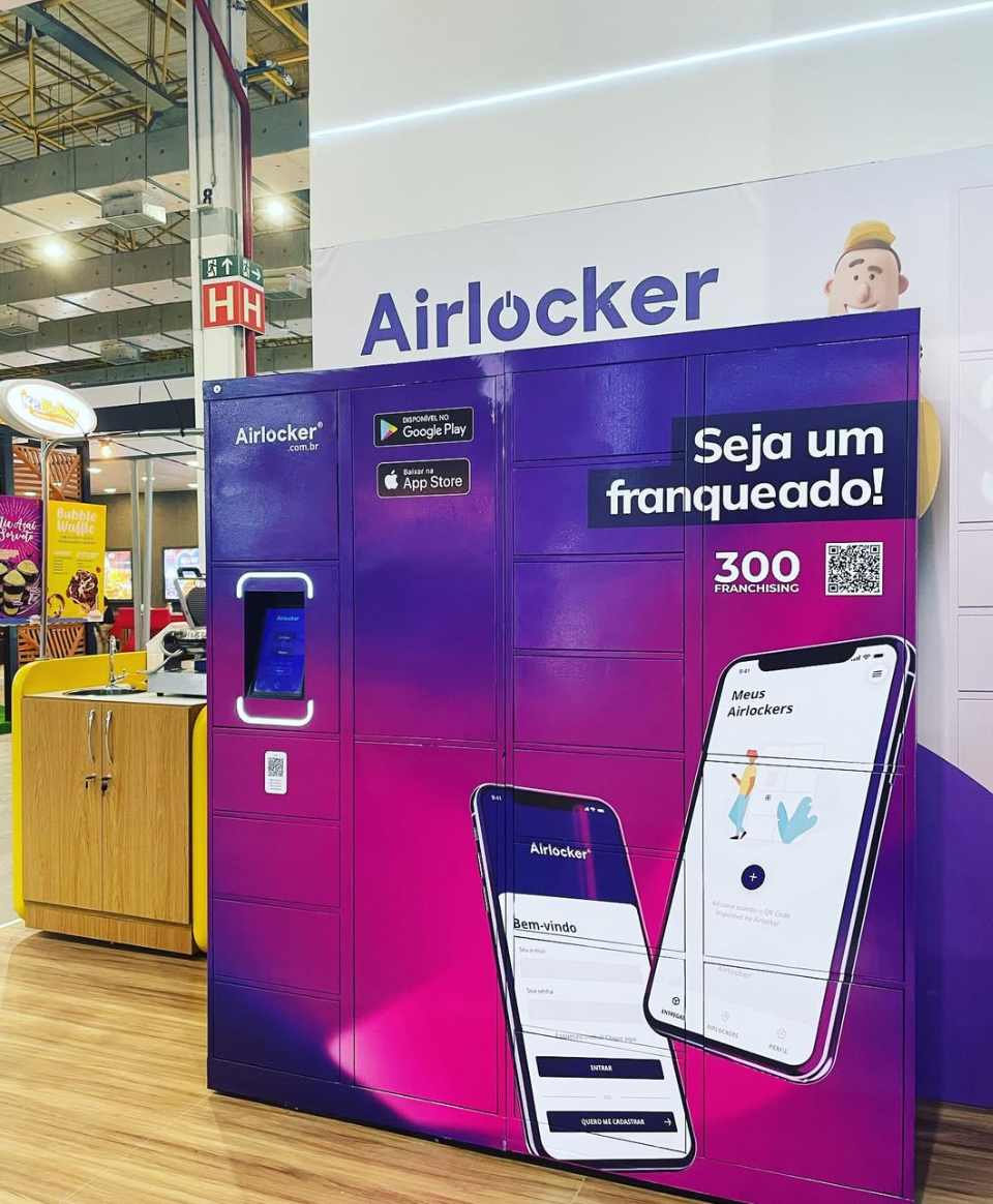 Armário Airlocker roxo em espaço de exposição, com telas demonstrativas do aplicativo